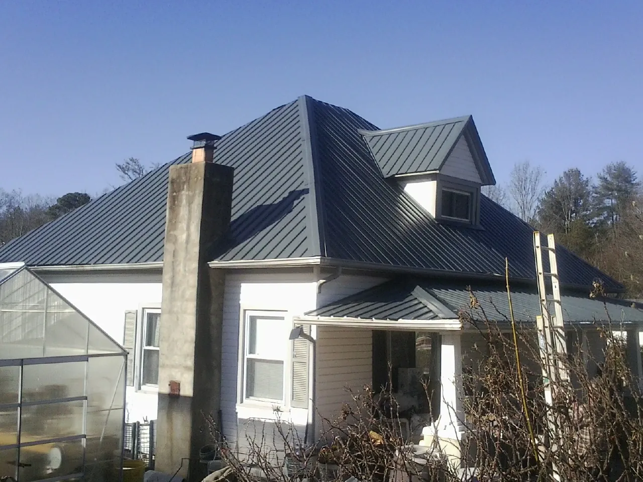 Dark blue standing seam metal roof on a white farmhouse with dormer — Slate & Tile Roof Repair by Roofing Brothers in Central City