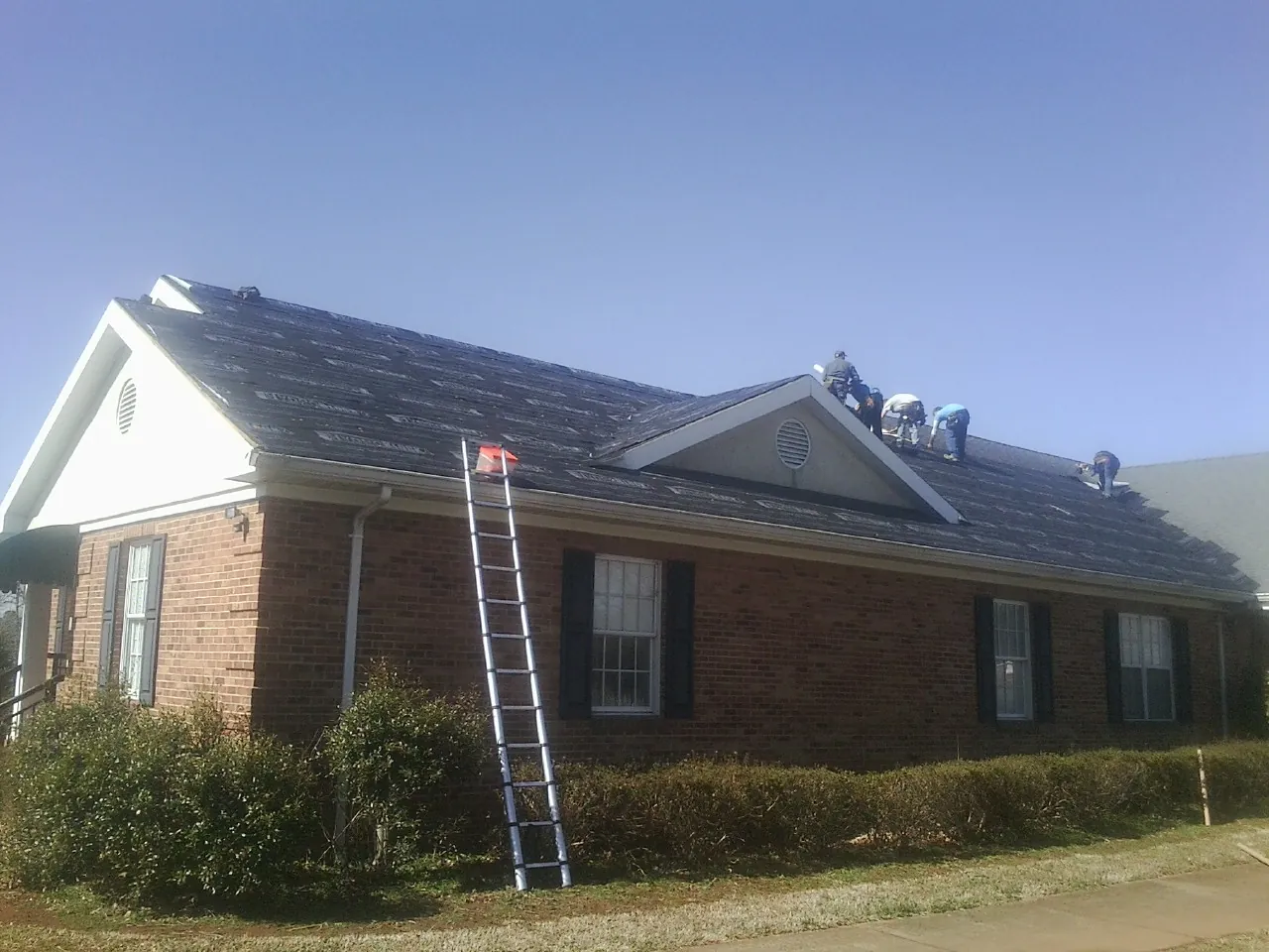 Crew tearing shingles off a brick ranch roof with a ladder set — Emergency Roof Repair work by our crew in Central City